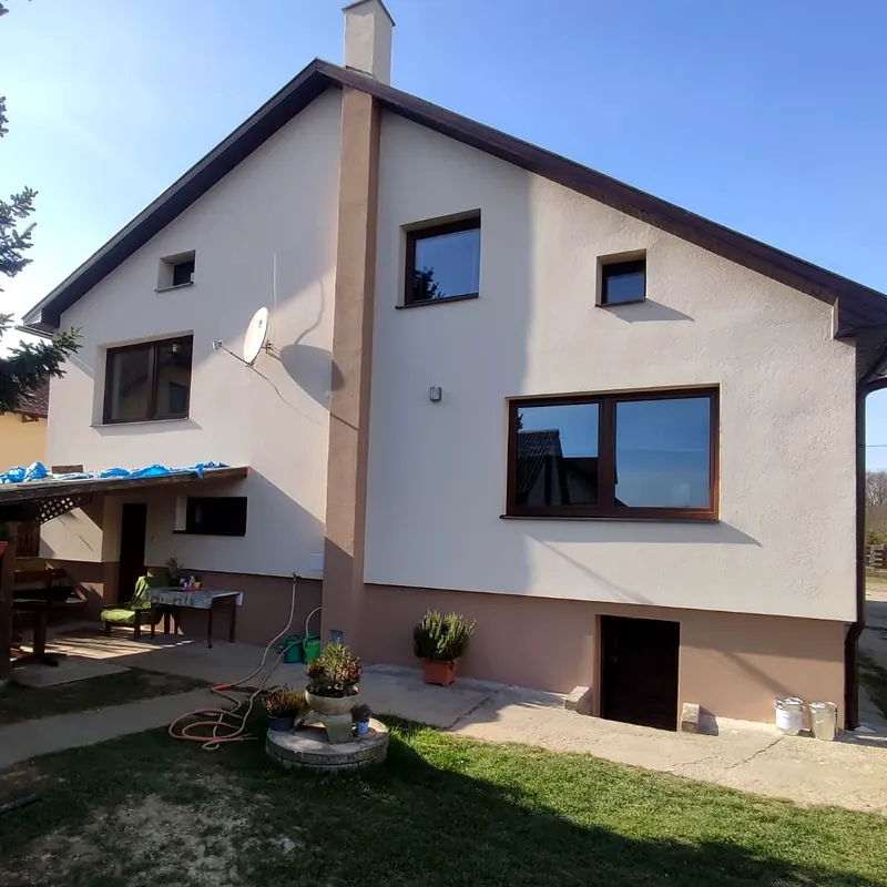 Rodinný dom po zateplení so svetlou fasádou a hnedým soklom, pohľad z dvora