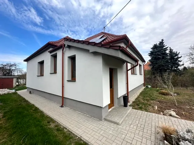 Zateplený prízemný dom s bielou fasádou, sivým soklom a červenou strechou