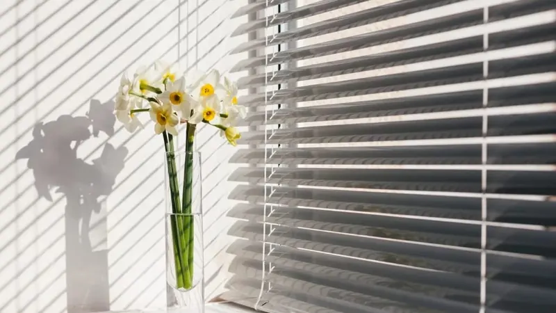 Horizontálne žalúzie a&nbsp;váza s&nbsp;narcismi pri okne